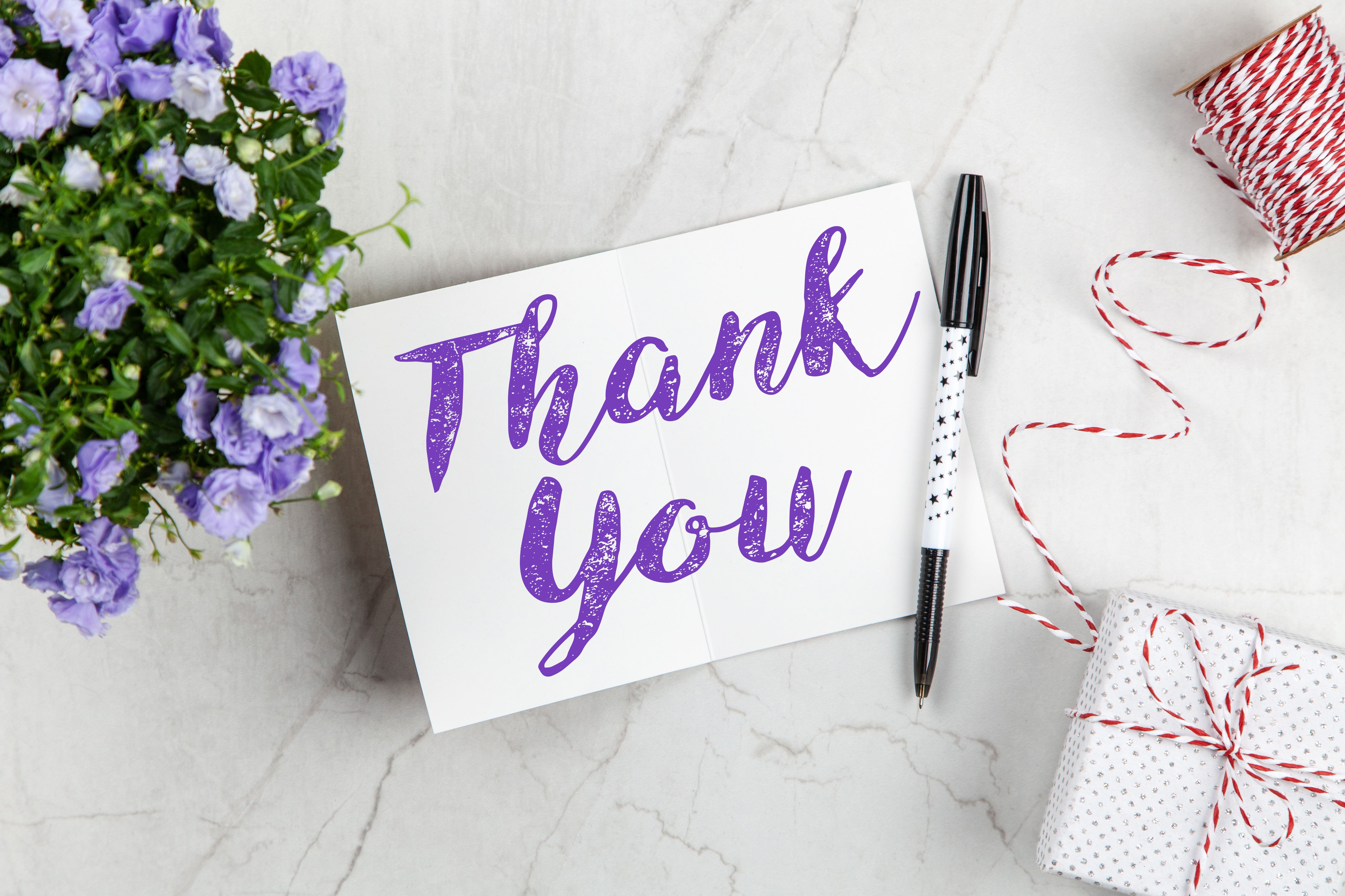 Elegant thank-you card displayed with purple flowers, a gift box, and a pen
