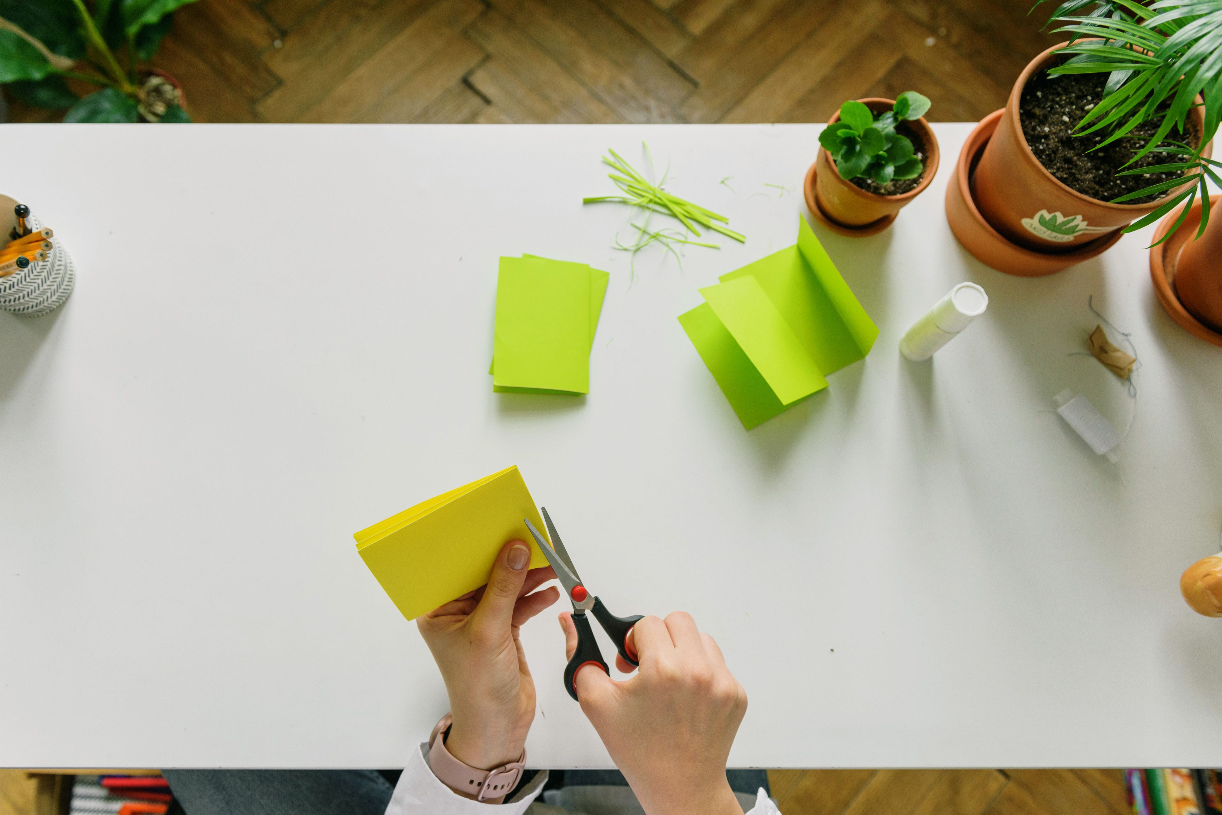 Hands cutting green paper with scissors on a bright craft workspace